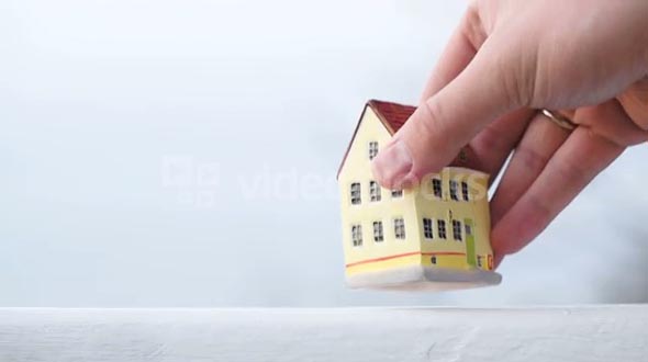 Hand putting a small toy house on the table on light background. Real estate or mortgage symbol