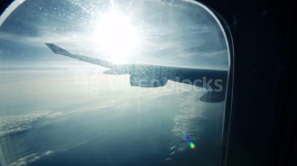 Scenic view from illuminator while traveling by air. Plane wing with sun flare and clouds beneath
