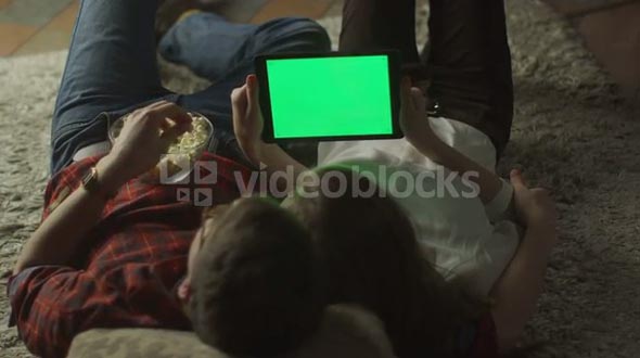 Young Couple are Laying on the floor and Watching Tablet PC with Green Screen at Home at Evening Time. Casual Lifestyle.