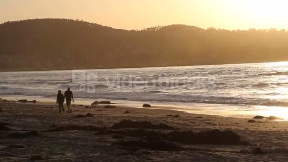Couple Walks On Ocean Beach At Sunset