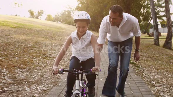 Father teaching daughter to ride her pink bike, steadicam shot.