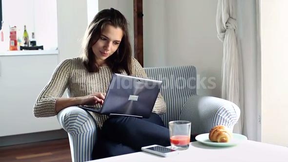 Woman sit in armchair and typing on modern laptop at home