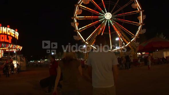 Couple Walks Through Carnival Near Ferris Wheel
