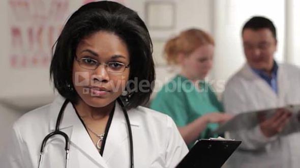 Confident female doctor looking at camera, nurse and doctor in background