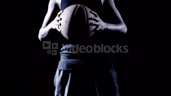 An African man dribbles a basket ball against a black background.