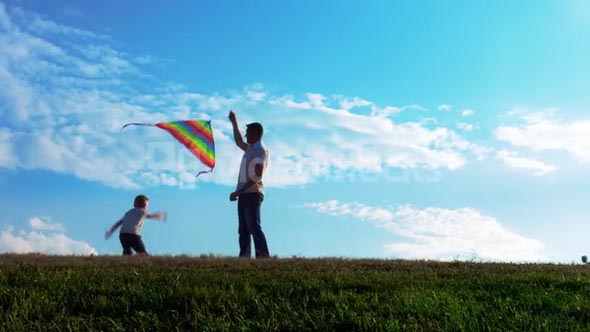 Father and son flying kite in open park with blue sky at sunset. Steadicam shot