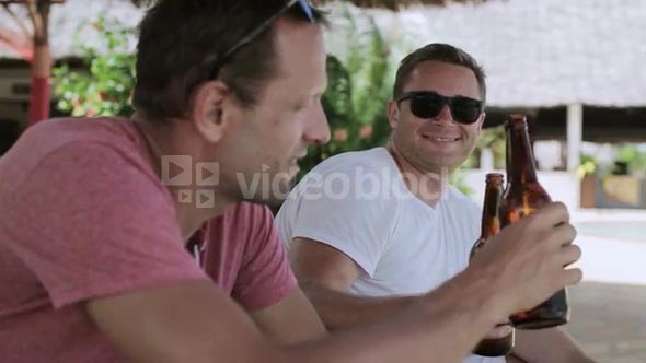 Men sitting on sunbeds and drinking beer, steadycam shot