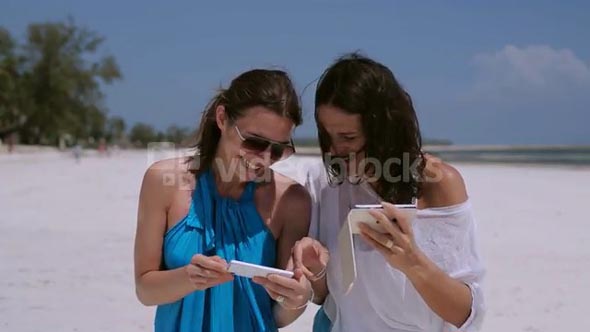 Happy women using cellphones on the beach
