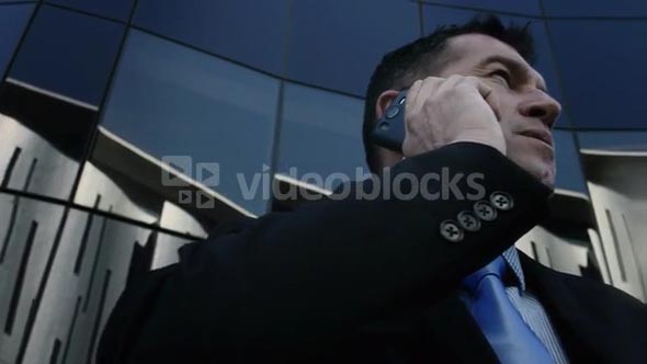 Suits business man talking on his mobile phone in modern glass city. Steadicam shot